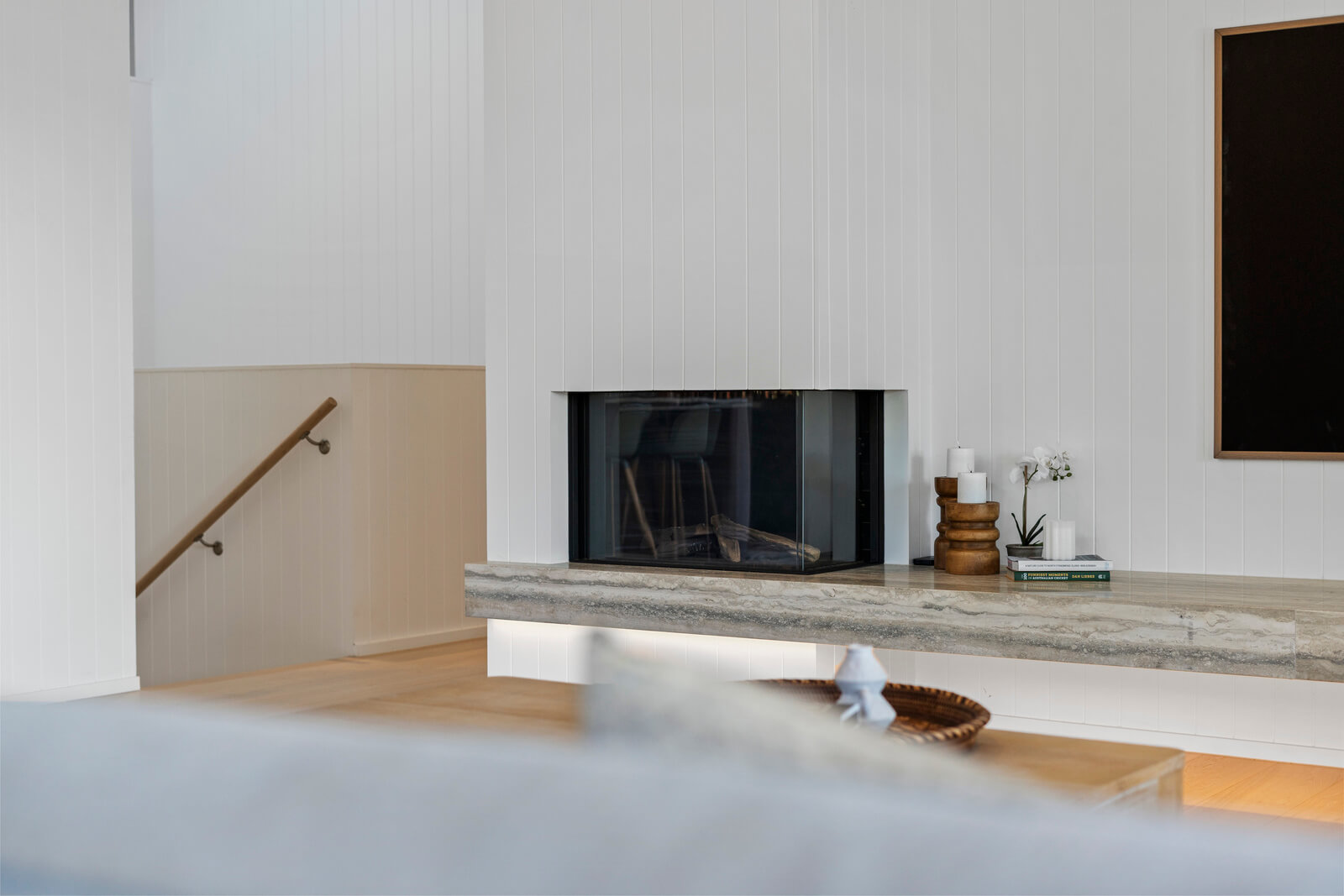 Contemporary coastal living room with fireplace, stone mantel, white walls, timber floors, and minimalist interior design.